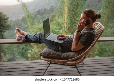 Young man using online banking for sending money everywhere you are from laptop, sit on terrace with mounain view