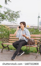 Young man using phone while sitting on bench with bicycle in park