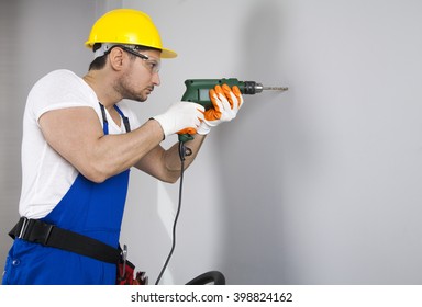 Young Man Using Power Drill On Wall At Home