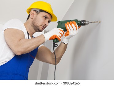 Young Man Using Power Drill On Wall At Home