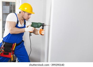 Young Man Using Power Drill On Wall At Home