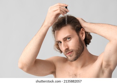 Young Man Using Serum For Hair Growth On Grey Background