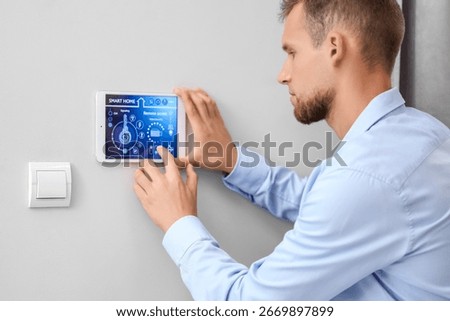 Young man using smart home control panel on light wall in room