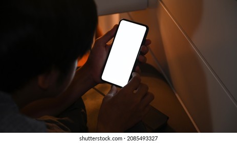 Young Man Using Smart Phone At Night While Lying On His Bed.