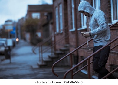 Young man using a smart phone before jogging and exercising on a sidewalk in the city