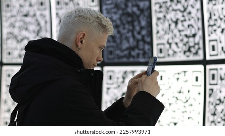 Young man using smartphone against wall with many qr codes at modern futuristic exhibition or museum. Education, technology, entertainment concept - Shutterstock ID 2257993971