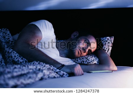 Young man using smartphone in bed at night