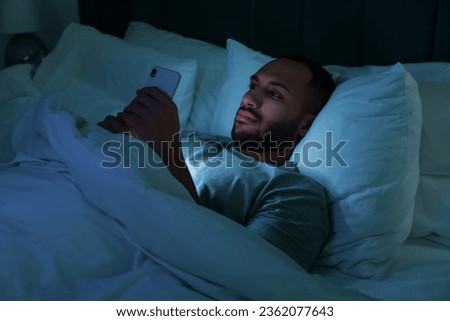 Young man using smartphone in bed at night. Internet addiction