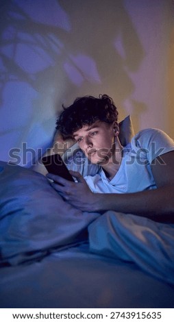 Young man using smartphone in bed at night with blue screen light. Concept of late night social media use, mobile apps engagement, digital consumption and screen time habits.