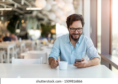 Young man using smartphone drinking coffee in a cafe 