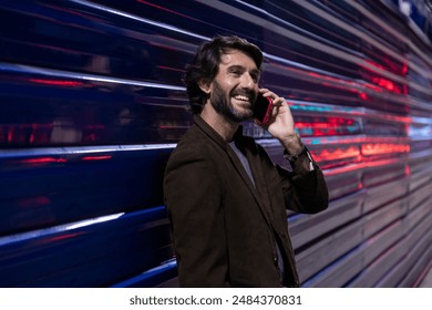 Young man using a smartphone at night time leaning against a blue wall with city lights.  Young man using a smartphone at night time  - Powered by Shutterstock