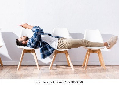 Young man using smartphone while lying on chairs in hall
