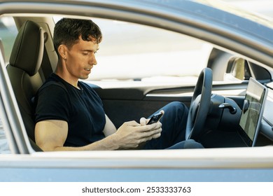 Young man is using a smartphone while sitting in the driver's seat of a parked car