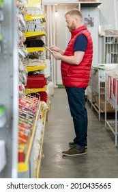Young man using tablet while making revision of goods on displays