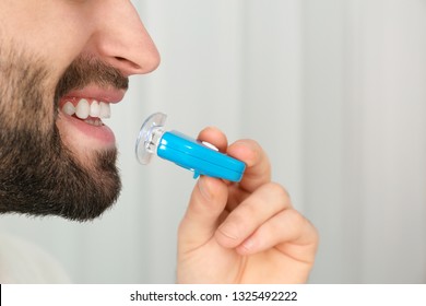 Young Man Using Teeth Whitening Device On Light Background, Closeup With Space For Text