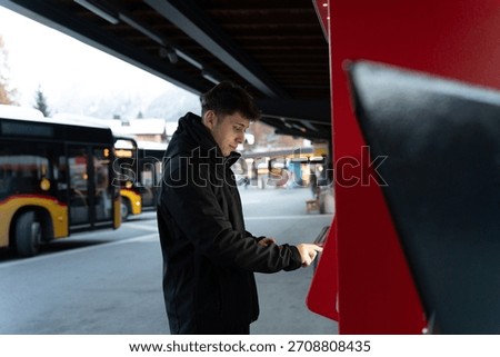 Young man using a ticket vending machine at a bus station in winter
