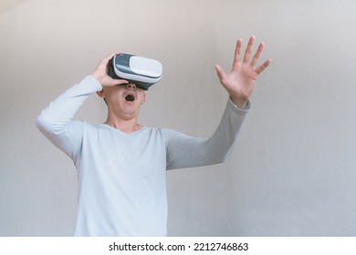 Young Man Using Virtual Reality Headset. Isolated On Grey Background Studio Portrait. VR, Future, Technology, Education Online, Studying . Man Trying To Touch Objects In Virtual Reality , 