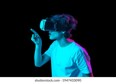 Young man using VR headset isolated over dark multicolored background in neon light. Future, gadgets, technology, education online concept. Human emotion, facial expressions 