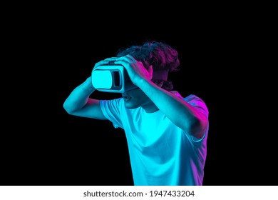 Young man using VR headset isolated over dark multicolored background in neon light. Future, gadgets, technology, education online concept. Human emotion, facial expressions. Copy space for ad.