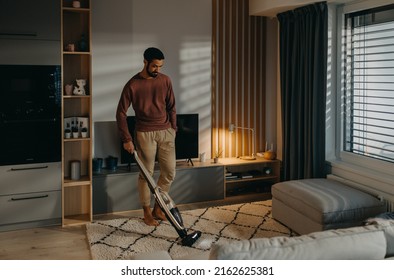 Young Man Vacuum Cleaning Carpet In Living Room