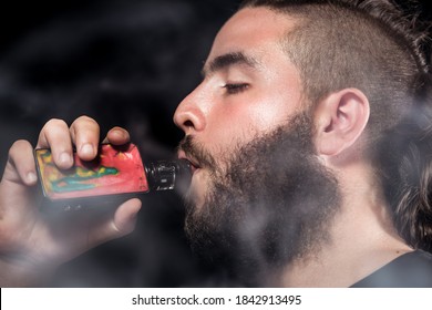 Young Man Vaping Electronic Cigarette In The Mouth Black Background With Smoke