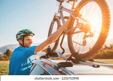 Young Man Veared In Cycling Clothes And Protective Helmet Instals His Mountain Bike On The Car Roof