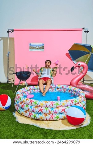 Young man in vibrant outfit with tropical shirt relaxing in inflatable swimming pool and cooking barbeque-sausages. Concept of pop art, travelling, party, recreation, lifestyle, fashion and style.
