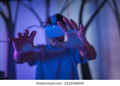 Young man with a virtual reality headset enjoying a multimedia experience in the dark VR room, a simulation of being in the forest.