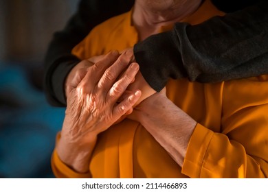 A young man, a volunteer, a son carefully hugs his beloved grandmother, supports and helps an elderly woman in retirement, his grandparent. Young male and female elderly hands with wrinkles closeup.  - Shutterstock ID 2114466893