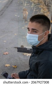 Young Man Waiting For Bus, At Bus Stop. Face Mask. Wearing Face Mask. Covered Face. 