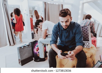 Young Man Waiting For Girlfriend In Dressing Room. Upset Man. Bearded Man. Woman On Shopping. Shopping In Modern Mall. Shopping Concept. Girl In Red Dress. Dressing Room In Boutique.