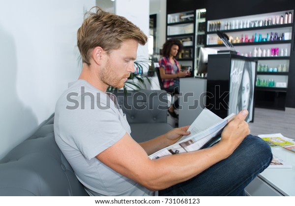 young man waiting in reception room reading magazine