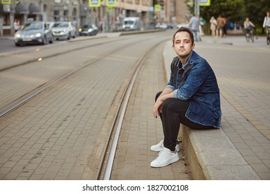 A Young Man Is Waiting For A Tramway At A Tram Stop. A White Male Sat Down On The Sidewalk Dangerously Close To The Train Tracks.