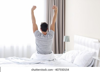 A young man waking up in bed and stretching his arms