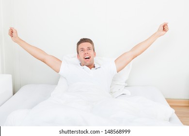Young Man Waking Up In Morning And Stretching On Bed