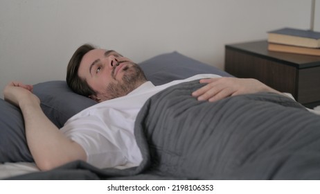 Young Man Waking Up From Nightmare In Bed