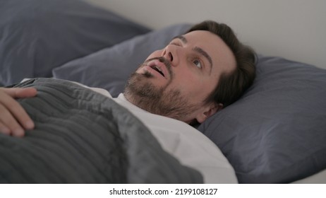 Young Man Waking Up From Nightmare In Bed