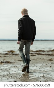 Young man walking alone on beach during low tide. Water and small hills in the distant background.