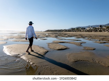 Young Man walking along beach near estuary with puddles of water in the sand