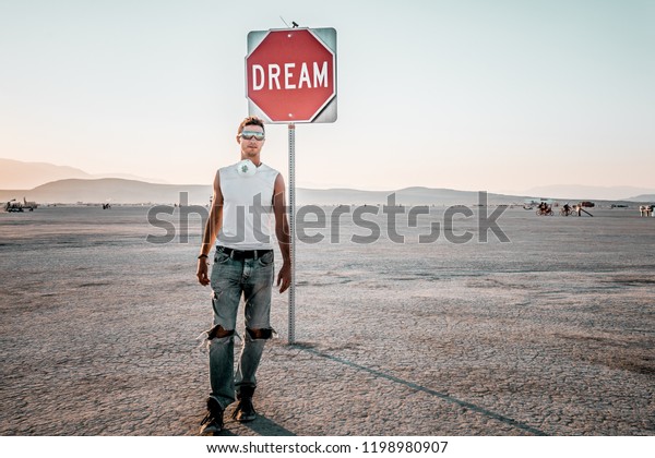 Young man walking by the dream sign in the\
middle of a desert at the Burning man - art and music festival.\
Sign to keep dreaming.