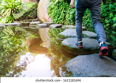 Young man walking crossing a river on stones.