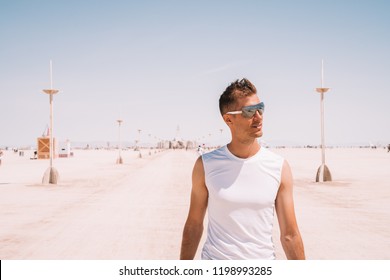 Young Man Walking Down The Desert In The Middle Of The Nowhere Between Lamp Posts At The Burning Man Festival.