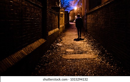 A Young Man Walking Home Alone At Night Through A Dark Alleyway In The UK.