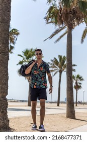 Young Man Walking On City Wearing Casual Clothes And Sunglasses With Shorts Flowered Shirt Holding Travel Bag