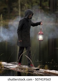 Young man walking on rustic wood planks holding an antique lamp at a rural lake.