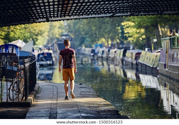 Young man walking on waterfront of Regents canal\
with boats
