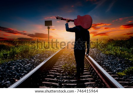 The young man walks along the railroad tracks in the light of the sunset.