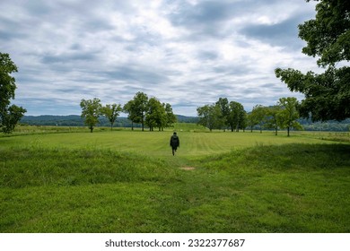 A young man walks toward the Native American Hopewell Culture prehistoric Seip Earthworks burial mound in Ohio. Ancient large long mound. Grass is neatly trimmed with trees dramatic sky. Copy space - Powered by Shutterstock