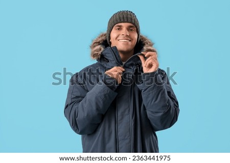 Young man in warm parka on blue background