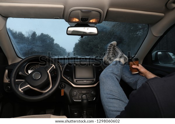 Young man in warm socks with coffee resting\
inside car, closeup